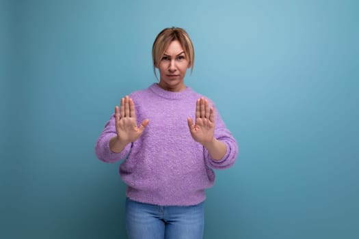 blonde woman in purple hoodie showing stop sign with hands on blue background.