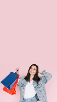 Joyful Shopper: Young Woman in Denim Shirt Celebrating, Arm Raised in Excitement, Against Pink Background, Delighted by Online Shopping or Amazing Find. Vertical photography