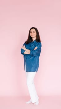 Portrait of professional businesswoman in smart casual attire standing confidently with folded hands, isolated on a pink background. Vertical photography