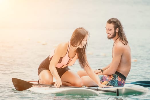 Sea woman and man on sup. Silhouette of happy young woman and man, surfing on SUP board, confident paddling through water surface. Idyllic sunset. Active lifestyle at sea or river