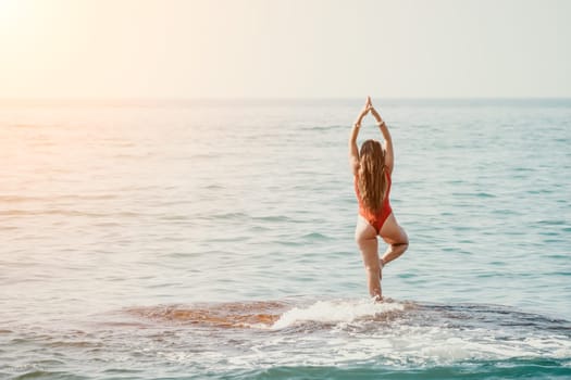 Woman sea yoga. Back view of free calm happy satisfied woman with long hair standing on top rock with yoga position against of sky by the sea. Healthy lifestyle outdoors in nature, fitness concept.