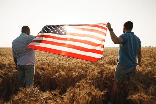 Two men patriots holding US flag above wheat field, back view