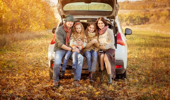 Happy family sitting in car trunk on autumn background