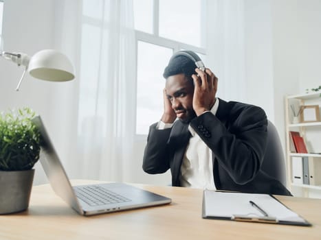 An African-American man sits at his desk in front of his laptop, wearing headphones and chatting on a video call, listening to music. The concept of student business training and online work. High quality photo