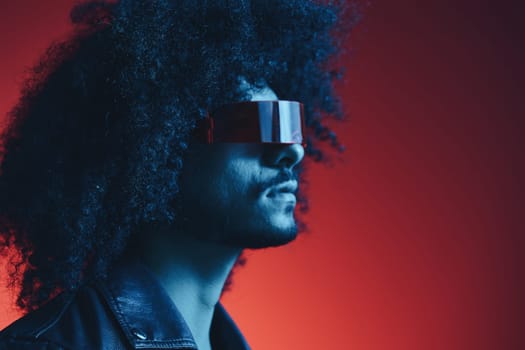 Portrait of fashion man with curly hair on red background with stylish glasses, multicultural, colored light, black leather jacket trend, modern concept. High quality photo