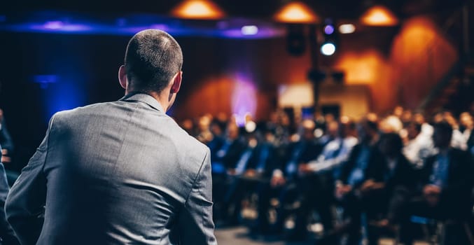 Speaker giving a talk on corporate business conference. Unrecognizable people in audience at conference hall. Business and Entrepreneurship event.