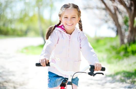 cuye little girl on her pink bike on the road. close-up