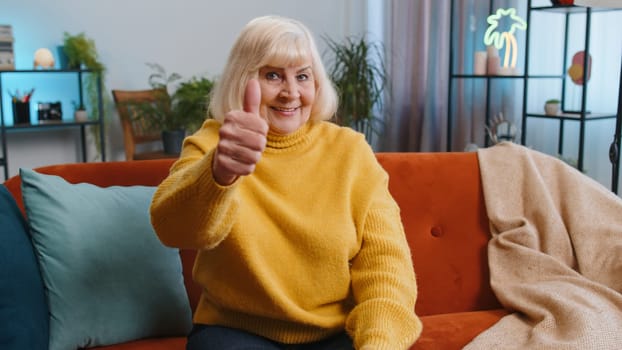 Like. Happy excited senior woman looking approvingly at camera showing thumbs up, like sign positive something, good great news, positive feedback. Elderly grandmother sitting on couch at home room