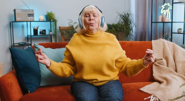 Keep calm down, relax, inner balance. Senior woman breathes deeply with mudra gesture, eyes closed, meditating with concentrated thoughts, peaceful mind at home. Elderly grandmother sitting on couch