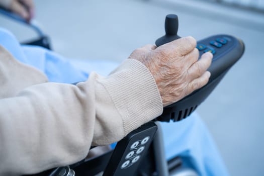 Asian senior woman patient on electric wheelchair with joystick and remote control at hospital.