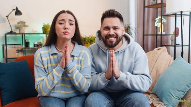 Please, God help. Young family marriage couple man woman praying sincerely with folded arms, looking upward and making wish, asking with hopeful imploring expression, begging apology. Husband and wife