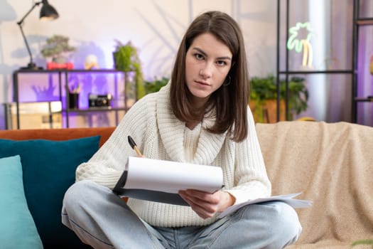 Woman freelancer work with documents from home, analyzing information, read business papers prepare financial report at home room apartment. Girl winner shocked by sudden victory, good success news