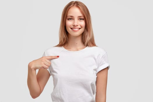 Clothing, design and advertising concept. Indoor shot of a positive young woman pointing to a copy space on her blank white t-shirt for your text or promotional content. download photo