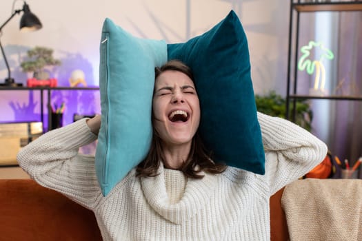 Repair work at neighbours. Irritated woman girl relaxing on couch cover ears with pillows annoyed by noisy neighbors suffer from headache wish silence. Thin walls at home flat without sound insulation