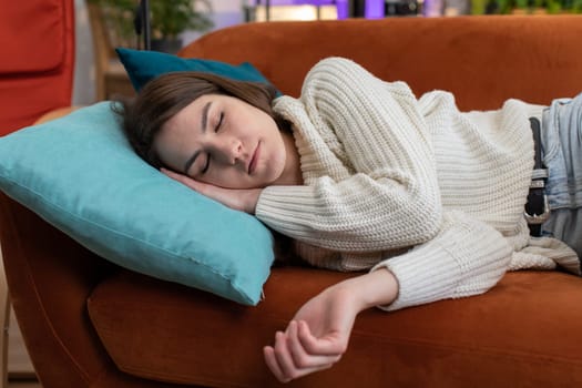 Tired young woman lying down in bed taking a rest at home apartment room. Carefree pretty girl napping, falling asleep on comfortable orange sofa with pillows. Closed her eyes enjoy daytime nap alone