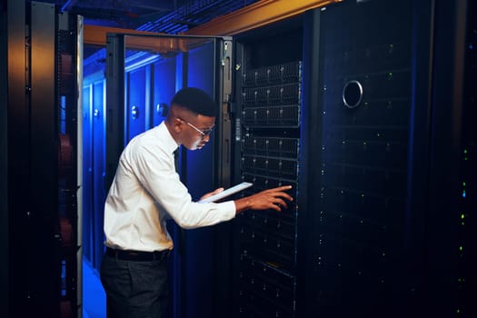 Going about the days inspections. a young man using a digital tablet while working in a server room