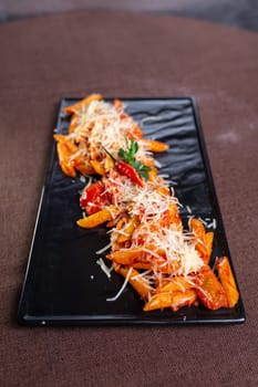 pasta with cheese and stewed tomatoes on a black plate.