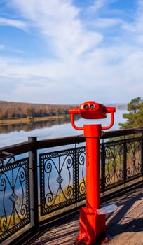 Public stationary binoculars on the banks of the river in summer or autumn to look at nature, coin-operated red metal binoculars.