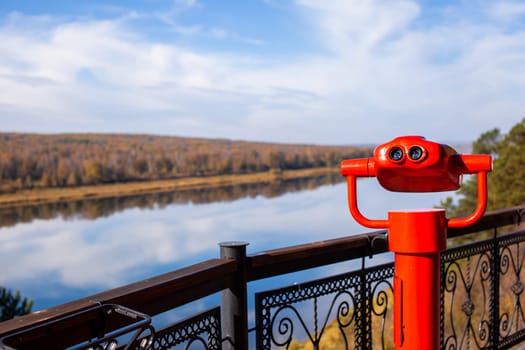 Public stationary binoculars on the banks of the river in summer or autumn to look at nature, coin-operated red metal binoculars.