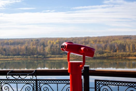 Public stationary binoculars on the banks of the river in summer or autumn to look at nature, coin-operated red metal binoculars.