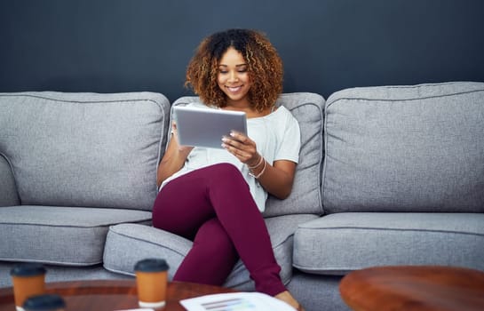 Comfortability inspires her productivity. a young businesswoman using a digital tablet on the sofa in a modern office