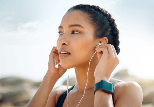 Woman with earphones, fitness at the beach and listening to music for motivation and workout outdoor. Exercise, health and wellness, female athlete streaming online with radio and audio in nature.