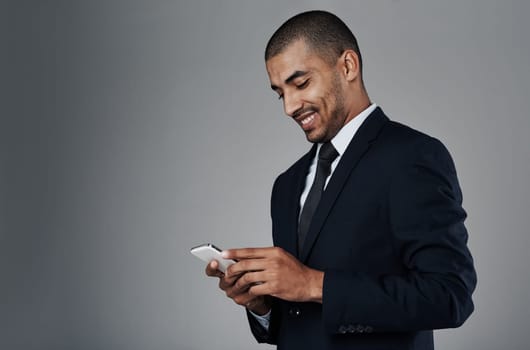 Staying aligned to business with technology. Studio shot of a corporate businessman texting on his cellphone against a grey background