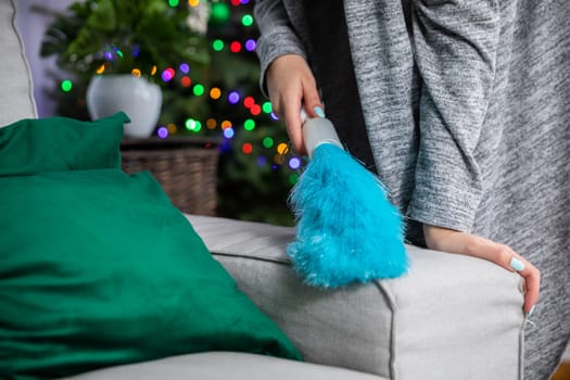 From the back of the sofa, a woman sweeps dust with a fine brush. Thorough cleaning for special occasions.