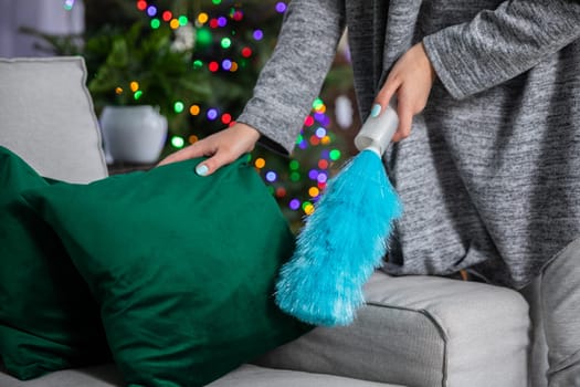 During a thorough cleaning, a woman picks up a pillow and sweeps up dust lying on the sofa. Taking care of order and tidiness throughout the house during all kinds of world.