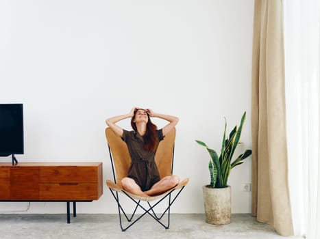 Woman sitting in a leather armchair near the window smiling , modern stylish interior Scandinavian lifestyle, copy space. High quality photo