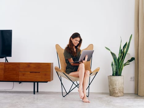 Female student study sits on a chair with a laptop work at home smile and relax, modern stylish interior Scandinavian lifestyle, copy space. High quality photo
