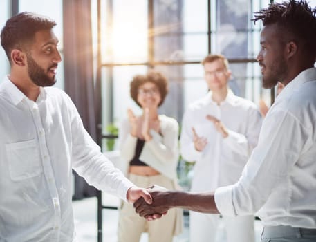 Glad to work with you. Young modern men in smart casual wear shaking hands and smiling while working in the creative office