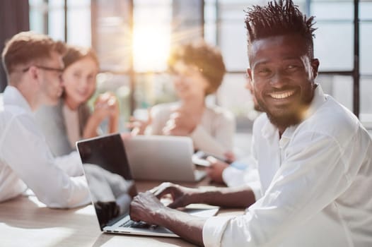 Portrait of smiling African American business man with executives working on laptop in background.