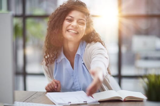 Happy young woman looking at the camera while welcoming a client. Smiling female executive manager, secretary offering professional business services