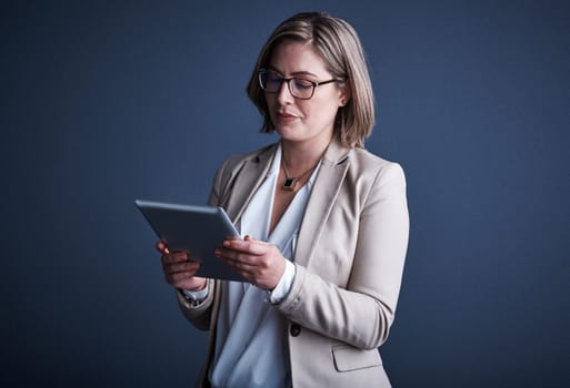 Taking a closer look. Studio shot of an attractive young corporate businesswoman using a tablet against a dark background