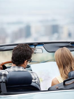 I think we should go this way next...Rear view of a young couple in their convertible checking a map