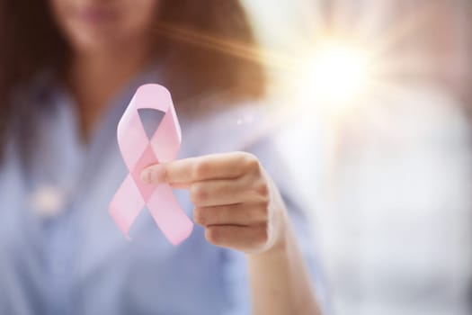 Young woman with pink ribbon smiling happily pointing with hand and finger