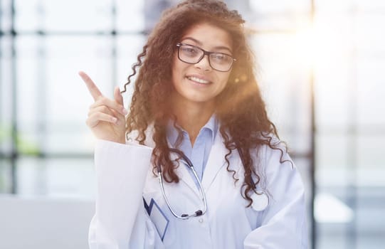 Portrait of an attractive young female doctor in a white coat points her finger