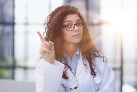 Portrait of an attractive young female doctor in a white coat points her finger