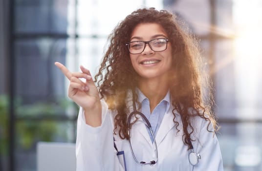 Portrait of an attractive young female doctor in a white coat points her finger
