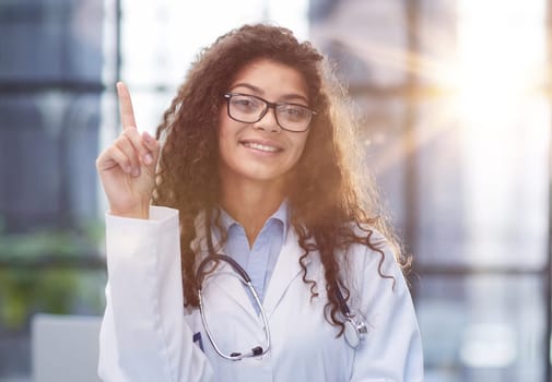 Portrait of an attractive young female doctor in a white coat points her finger