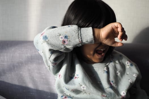 a upset child girl cover her face with hand .