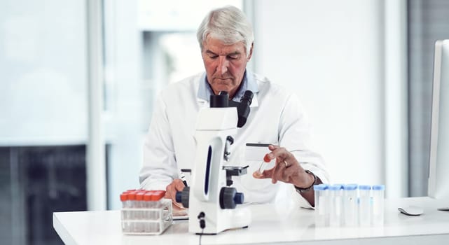 Looks like this is the last vile. a focused elderly male scientist holding up a test tube and making notes while being seated inside of a laboratory