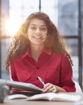 Attractive young business woman, writing notes to notebook at her workplace in office.