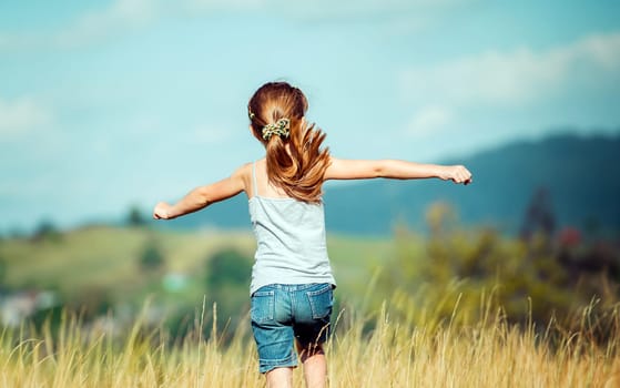 little girl runs through a beautiful meadow in the mountains. back view