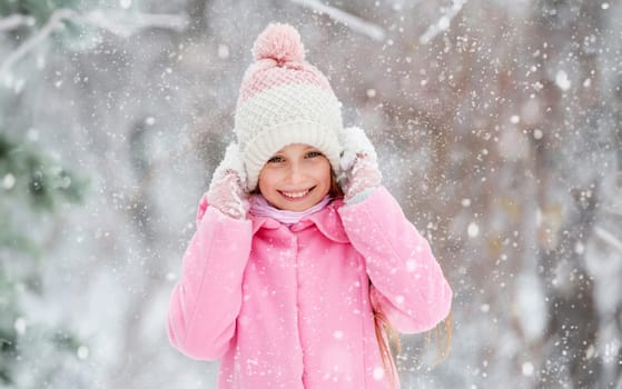 Lovely girl grinning widely and happily in the winter forest, holding her hat