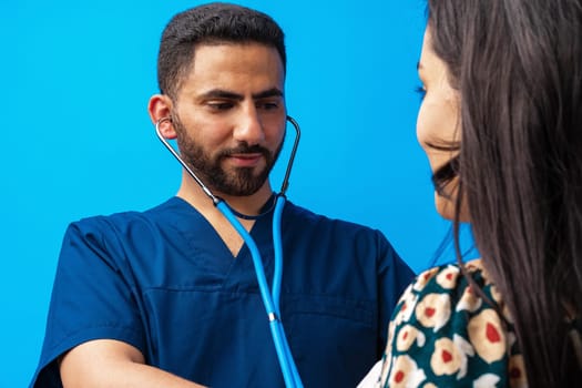 Arab doctor in a blue uniform standing with the stethoscope and listening to the heartbeat of a woman patient, close up