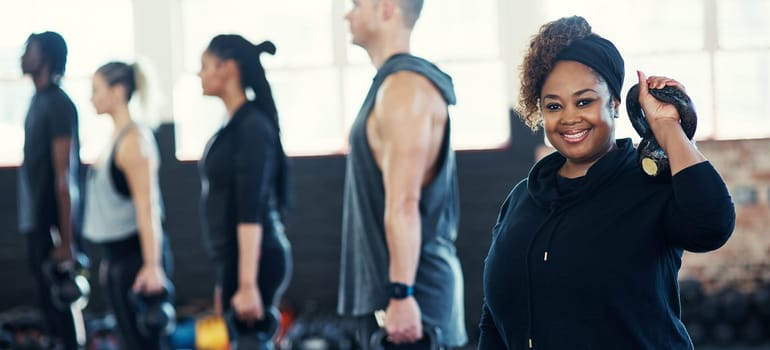 All about that fitness. a cheerful group of young people standing in a row and training with weights while one looks into the camera in a gym