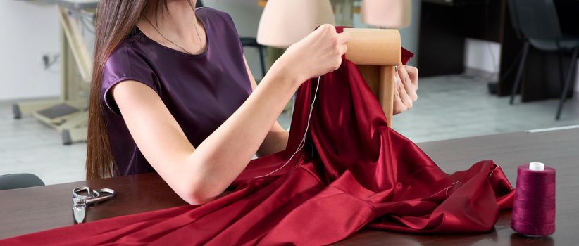 Beautiful young dressmaker in workroom sewing red dress