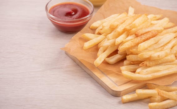 Golden yummy deep French fries on kraft baking sheet paper and serving tray to eat with ketchup and yellow mustard, close up, lifestyle.